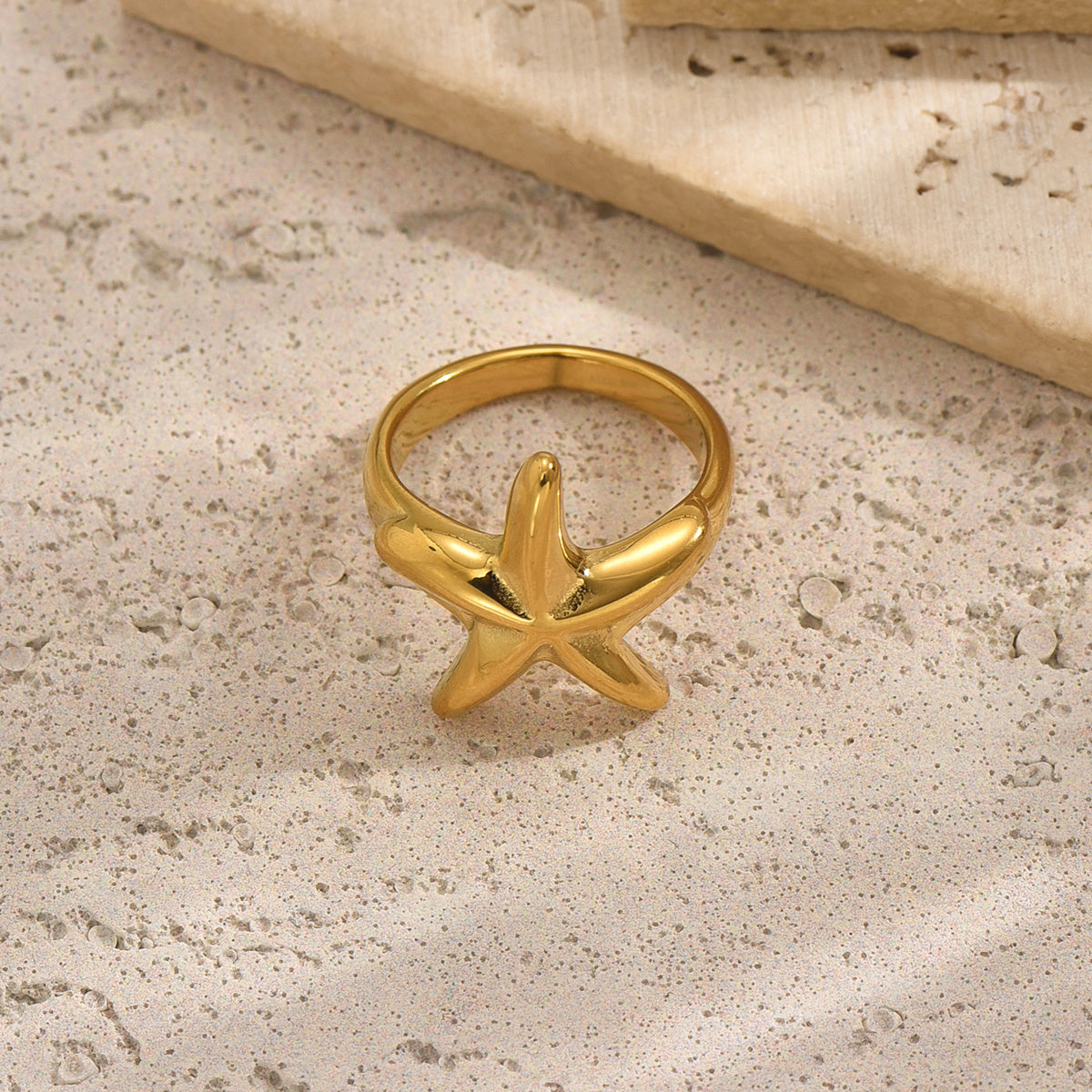 Gold starfish ring on a textured beige surface