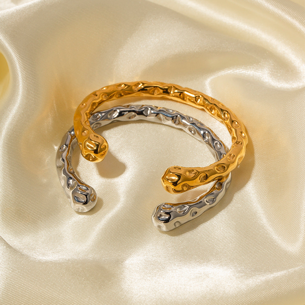 A gold and a silver textured bracelet rest on smooth, light-colored fabric.