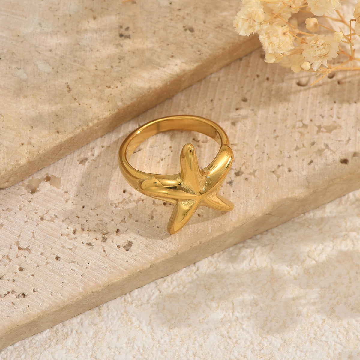 Gold ring with starfish design on a beige stone surface