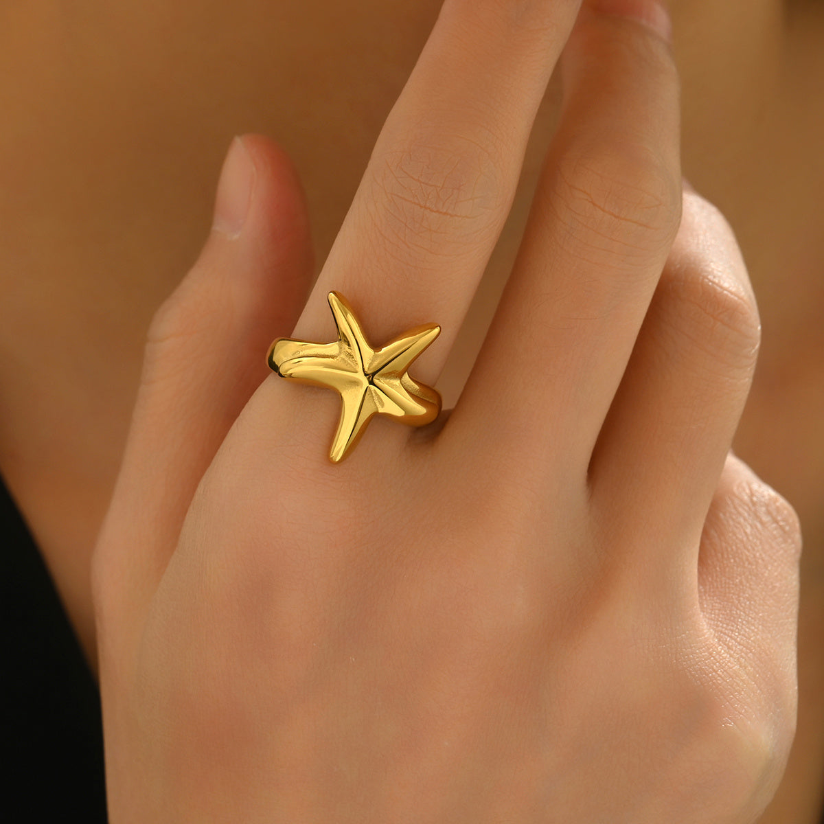Gold starfish ring on a hand against a neutral background