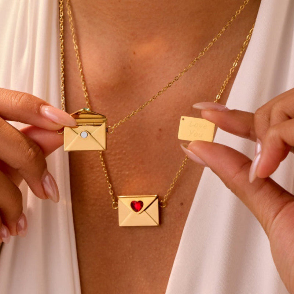 Person wearing a gold necklace with envelope pendants, holding one in each hand.