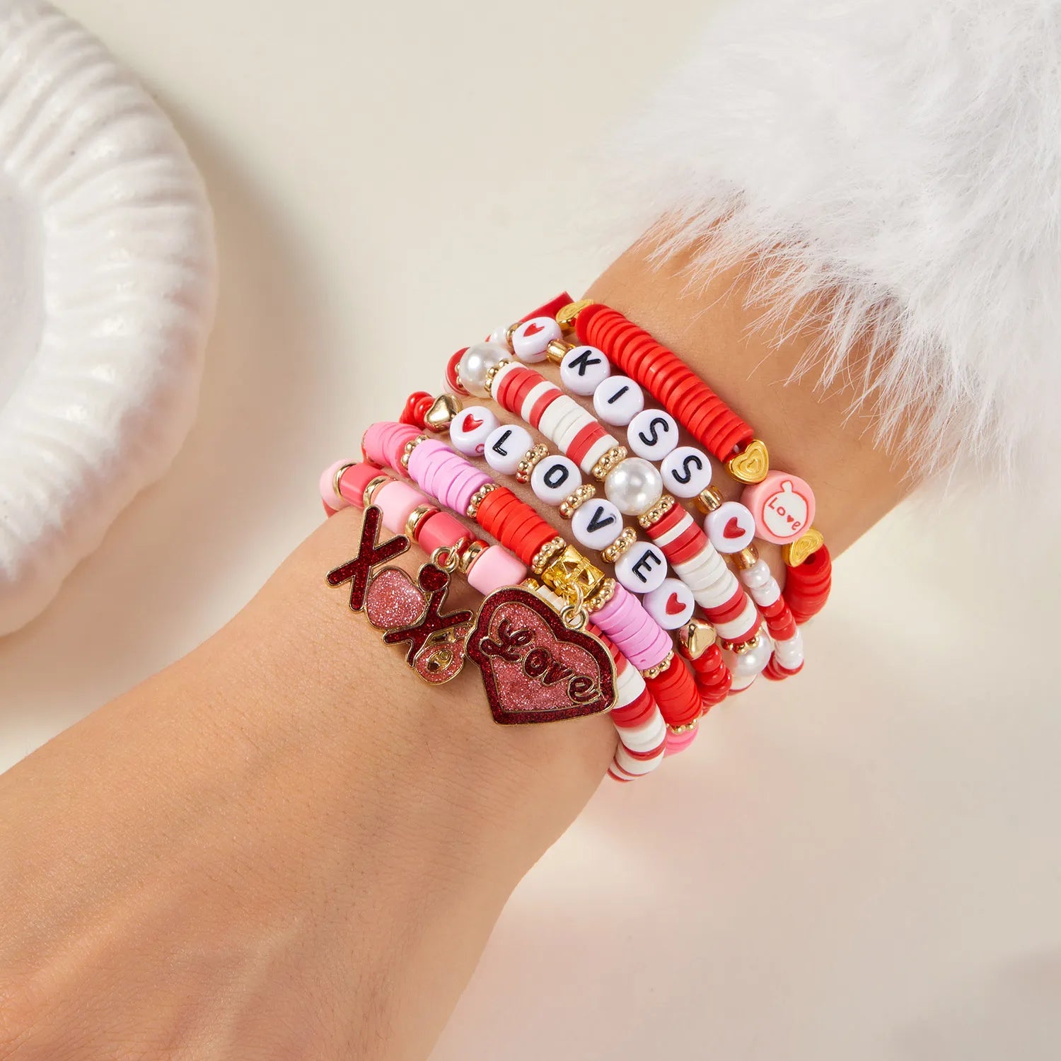 Wrist wearing multiple colorful bracelets with letters and charms on a light background