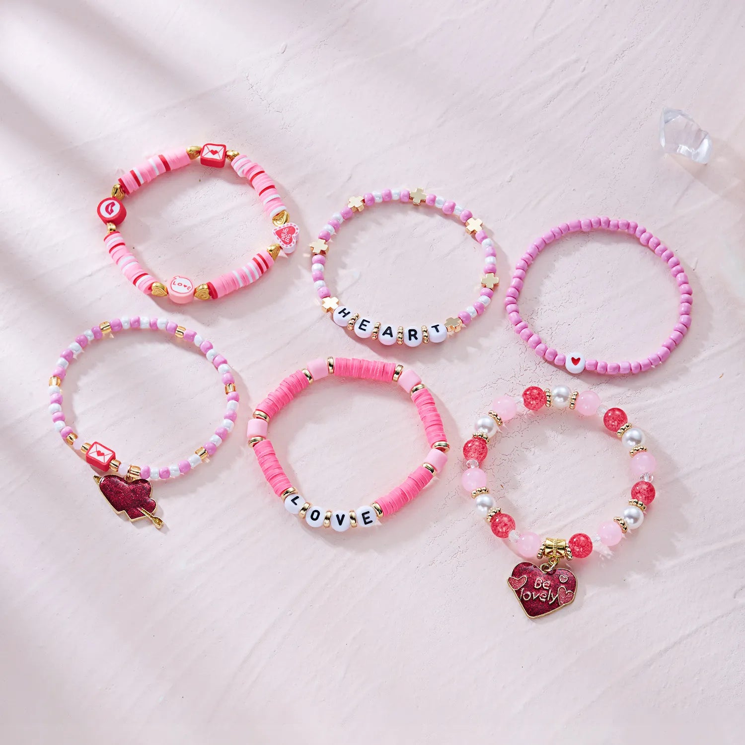 Set of pink beaded bracelets with various charms on a light pink fabric background