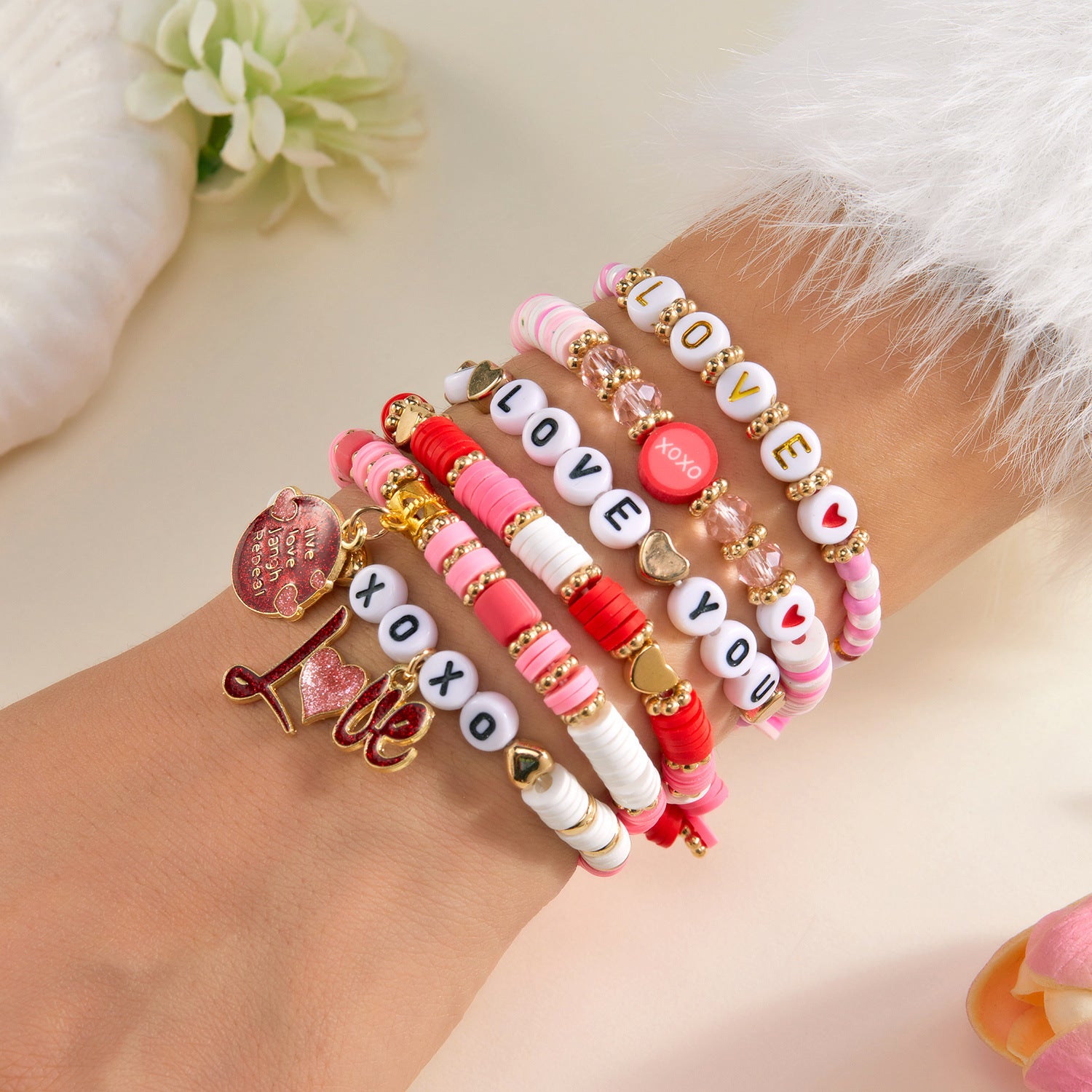 Set of colorful beaded bracelets with 'LOVE' and heart charms on a wrist, with a soft background.