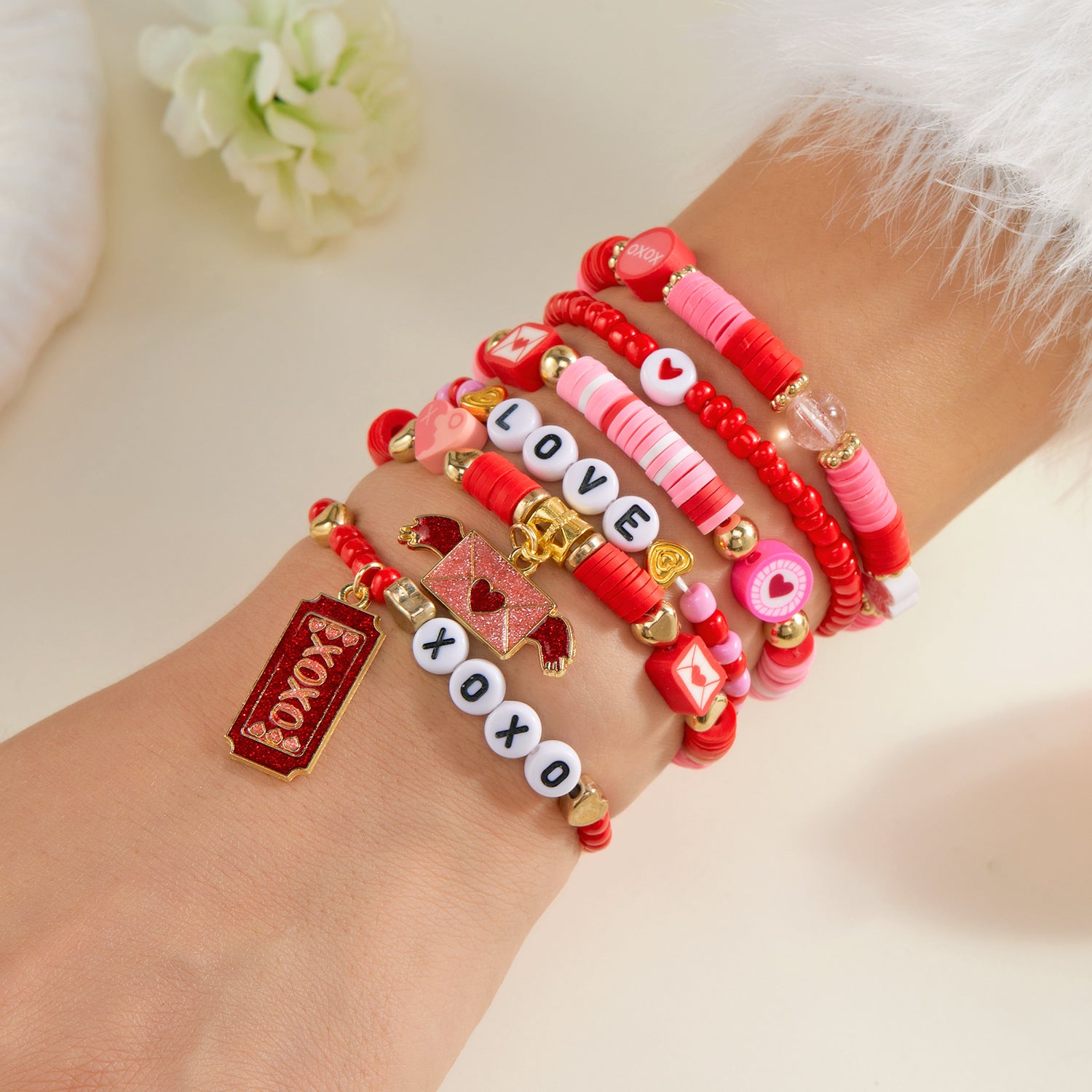 Hand wearing multiple colorful bracelets with letters and charms on a light background