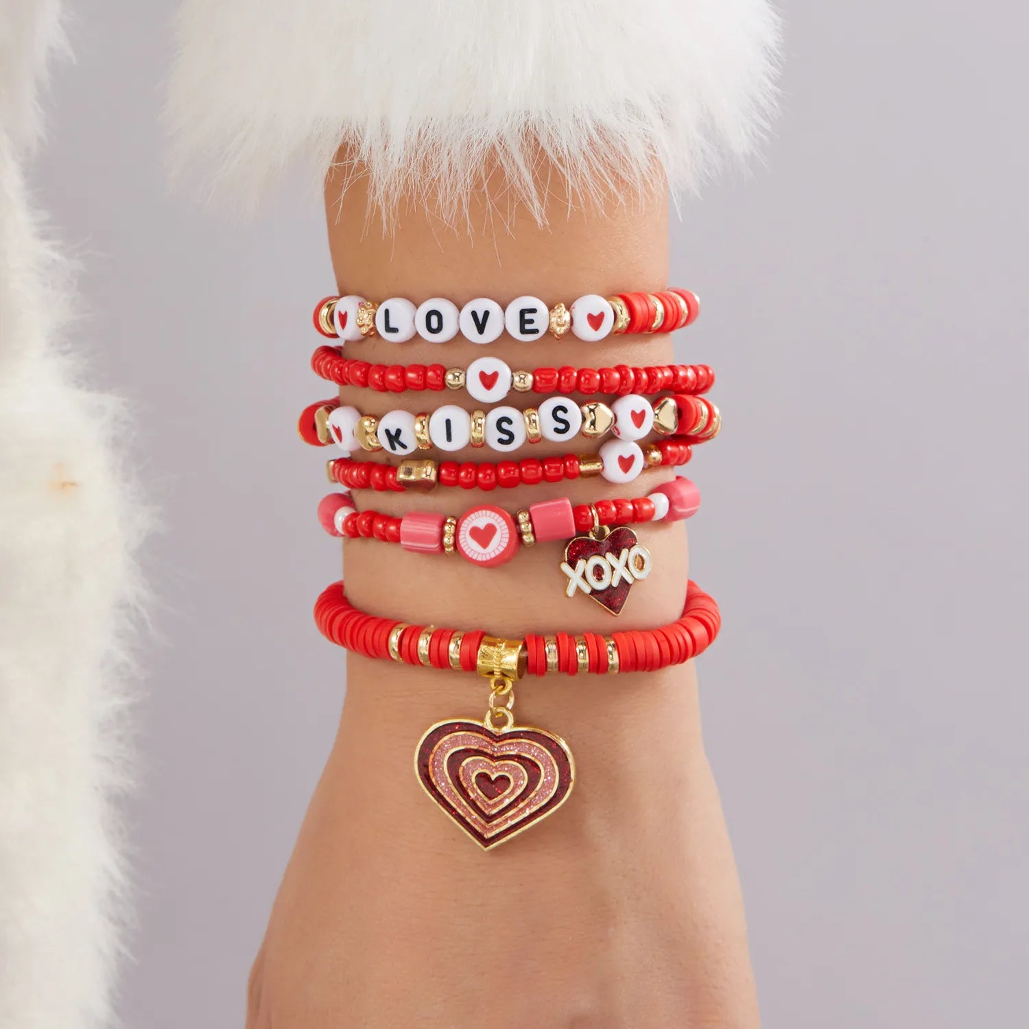 Multiple red and pink beaded bracelets with charms on a wrist against a light gray background