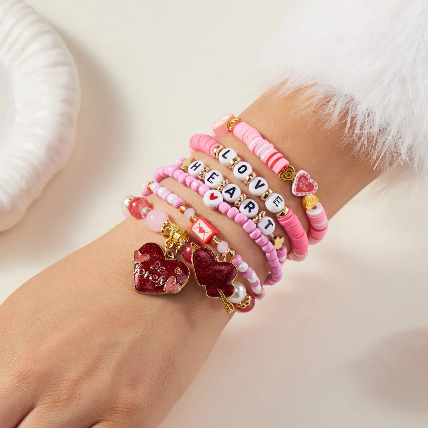 Multiple pink and red beaded bracelets with heart charms on a wrist against a white background