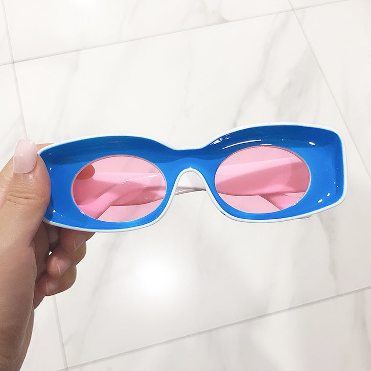 A pair of pink retro square candy sunglasses held in a person's hand, with a marble background.