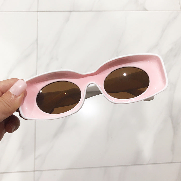 A pair of pink retro square candy sunglasses held in a person's hand, with a marble background.