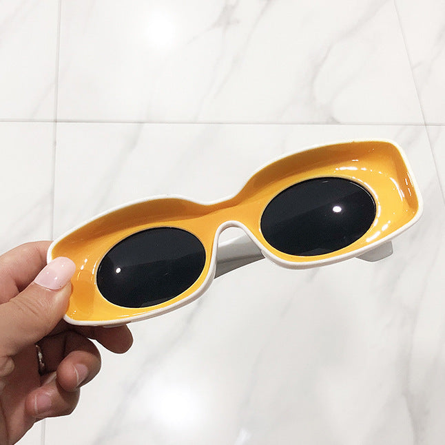 A pair of pink retro square candy sunglasses held in a person's hand, with a marble background.