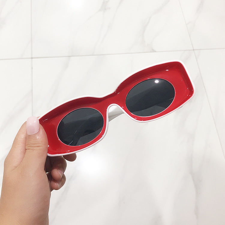 A pair of pink retro square candy sunglasses held in a person's hand, with a marble background.