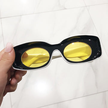 A pair of pink retro square candy sunglasses held in a person's hand, with a marble background.