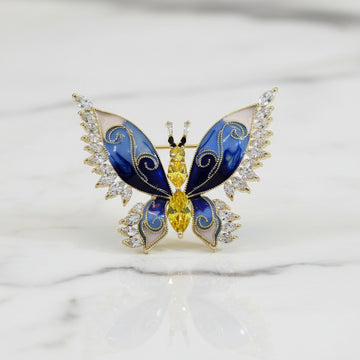 Butterfly-shaped brooch with blue wings and yellow body on a marble surface