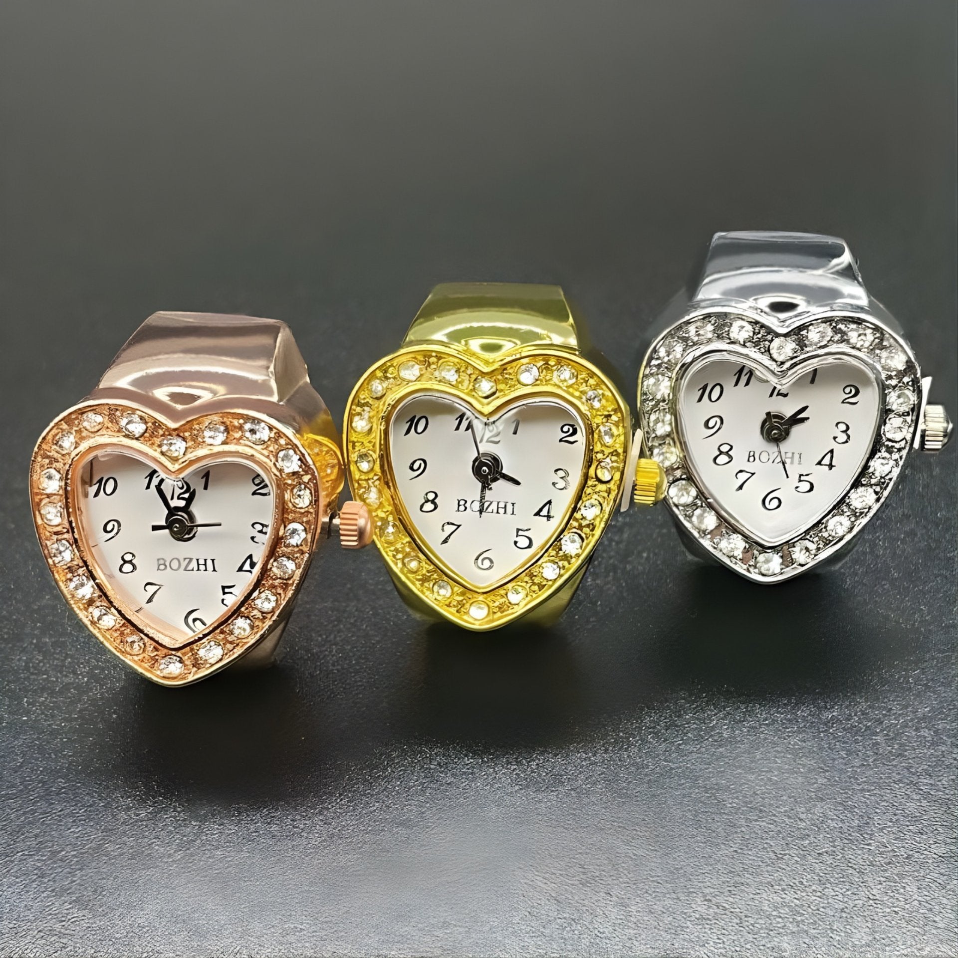 A collection of heart-shaped ring watches with sparkling crystals, displayed in gold, silver, and rose gold colors.