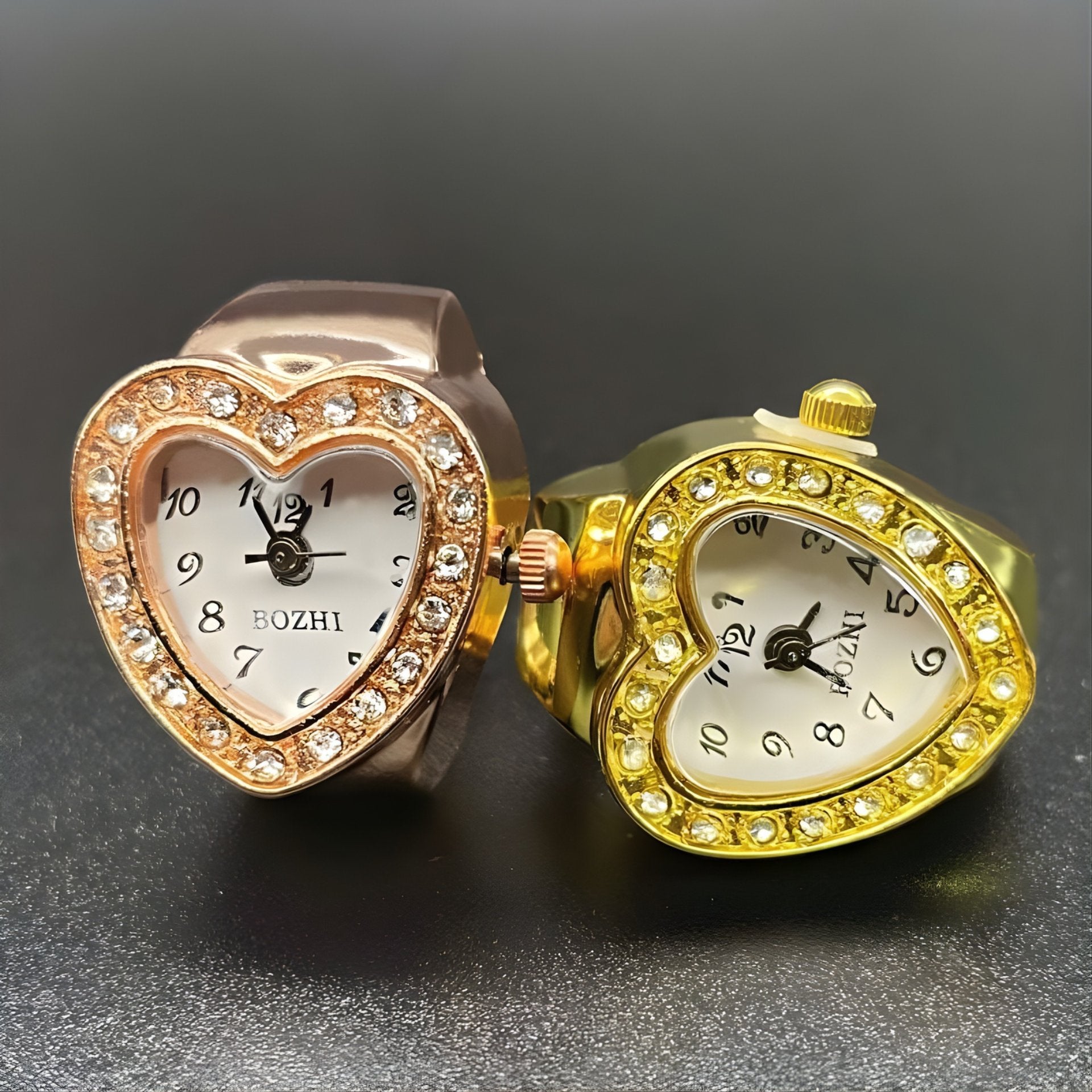 A collection of heart-shaped ring watches with sparkling crystals, displayed in gold, and rose gold colors.