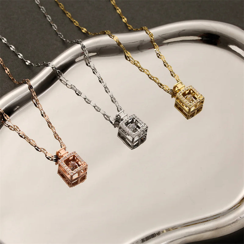 Three square pendant necklaces in gold, silver, and rose gold on a reflective surface.