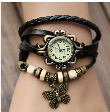 Vintage-style wristwatch with leather strap and butterfly charm on a wrist.