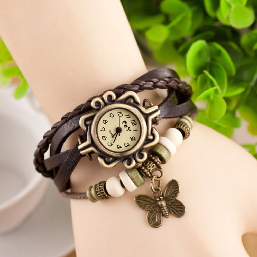 Bracelet with butterfly charm on wrist against a blurred green background