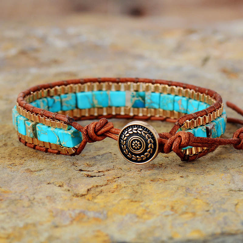 Turquoise beaded bracelet with brown leather strap and decorative button on a stone surface