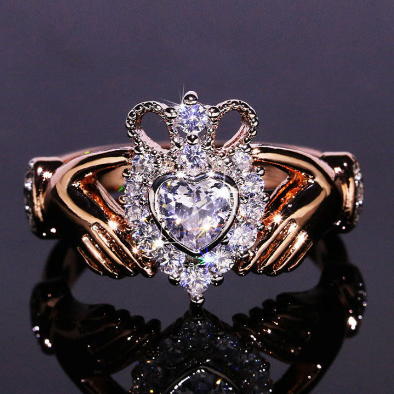 Gold ring with a heart-shaped diamond and crown design on a reflective surface.