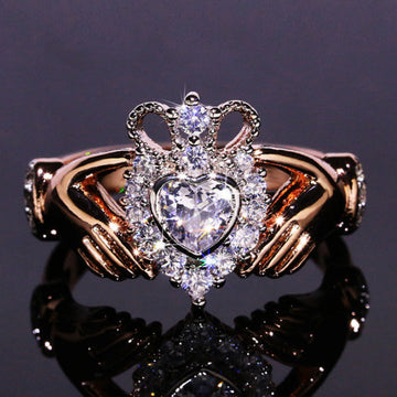 Gold ring with a heart-shaped diamond and crown design on a reflective surface.