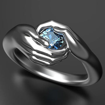 Silver ring with a blue gemstone held between two hands on a dark background