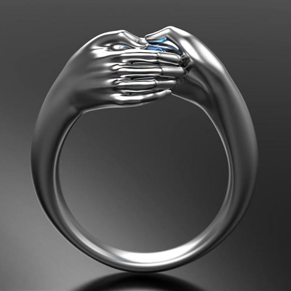 Silver ring with a design of two hands holding a blue gemstone on a dark background