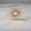 Gold sun-shaped brooch with gemstones on a marble surface