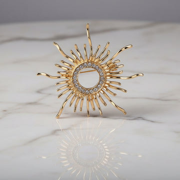 Gold sun-shaped brooch with gemstones on a marble surface