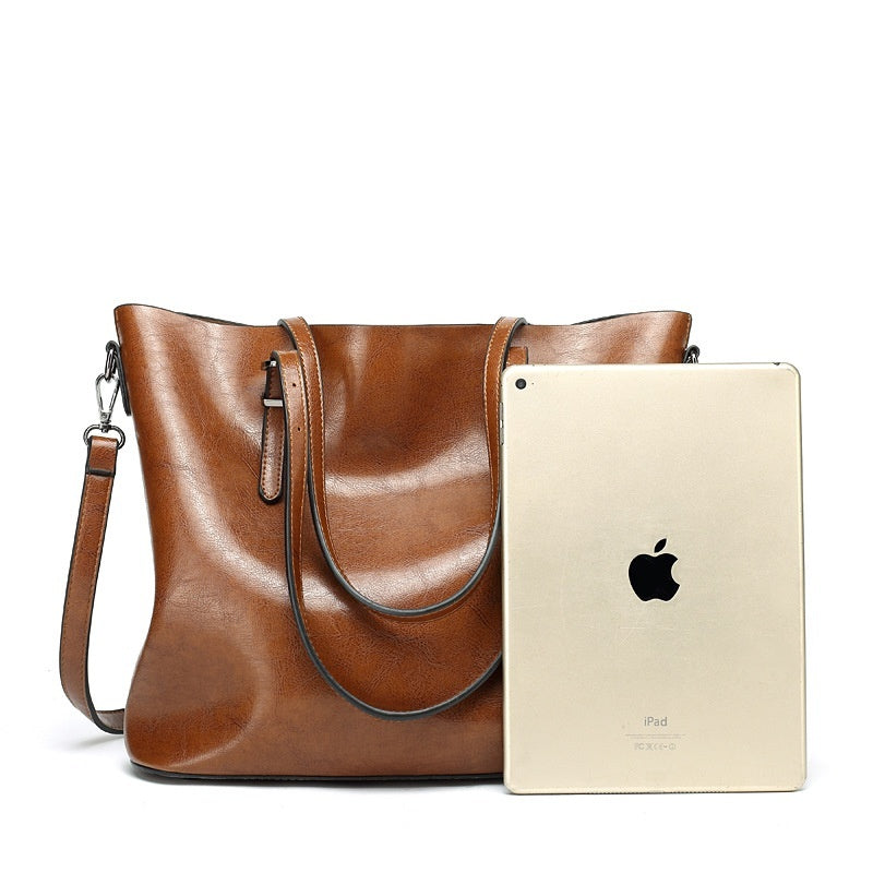 Brown leather handbag next to a gold iPad on a white background