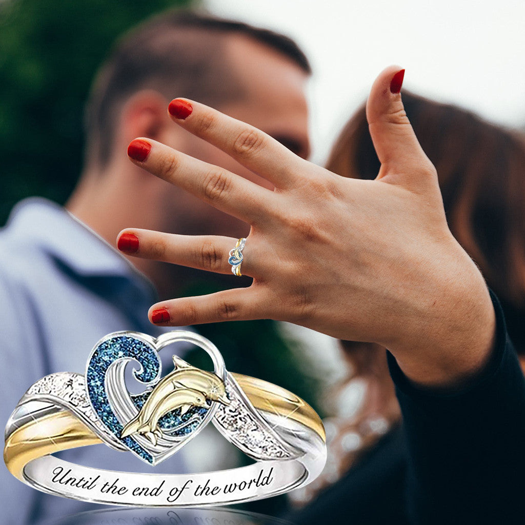Two rings with dolphins and 'Until the end of the world' engraving, one worn on a hand.
