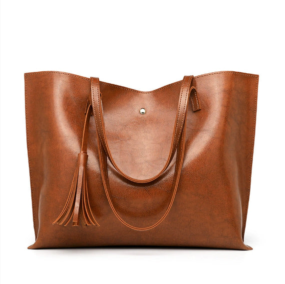 Brown leather tote bag with tassels on a white background