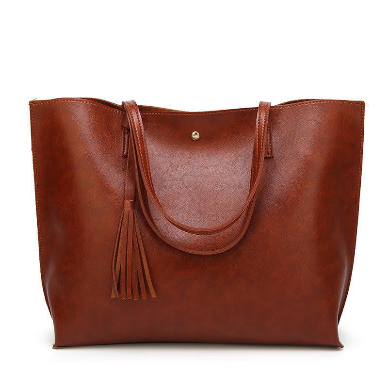 Dark brown leather tote bag with a tassel on a white background
