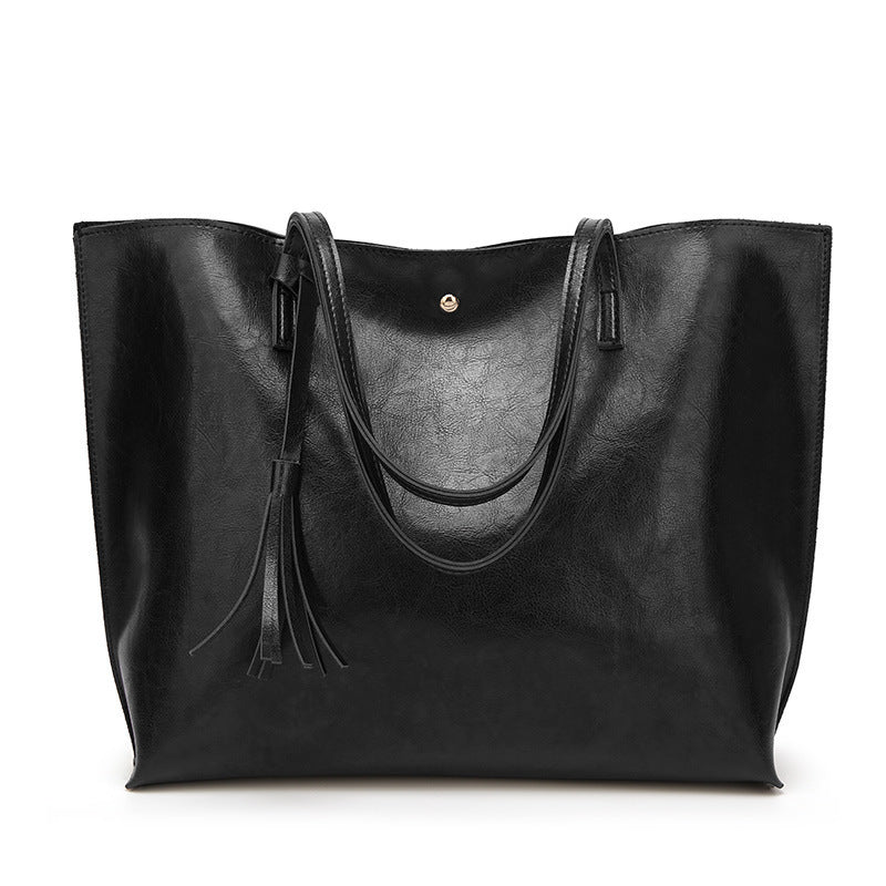 Black leather tote bag with tassels on a white background